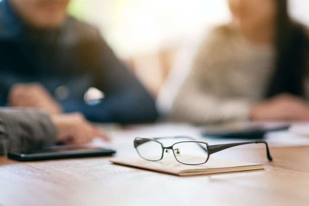 Close up image of black eyeglasses on notebook with blur businessman in office