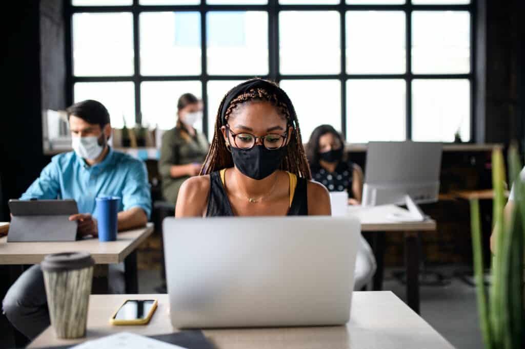 Portrait of young businesspeople with face masks working indoors in office